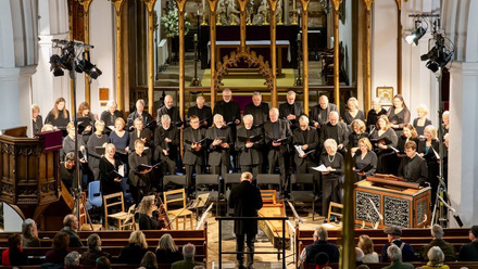 Choir singers all dressed in black face the composer. People observe from the foreground.
