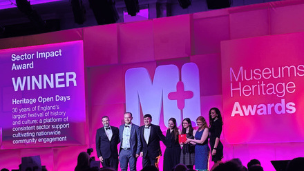 7 people stood on a pink lit stage receiving an award.