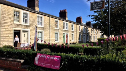 A line of stone cottage buildings, one has been turned into a museum. Outside is a HODs open day sign next to the Museum signpost.