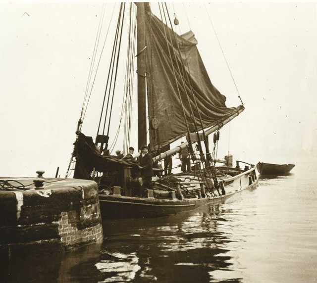 Wide, flat boat with large sail.