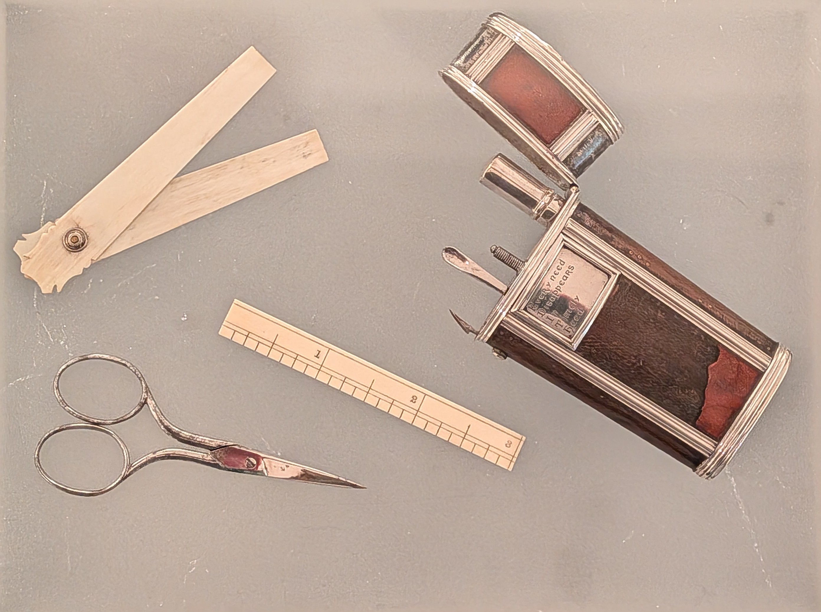 Small wood and metal case with hinged top open and objects scattered around including nail scissors and a ruler.