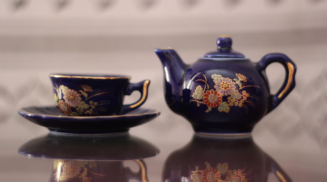 A dark blue decorated tea pot and tea cup with saucer.