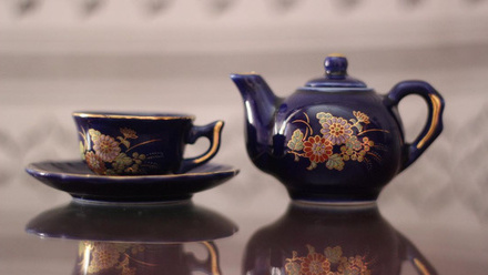 A dark blue decorated tea pot and tea cup with saucer.