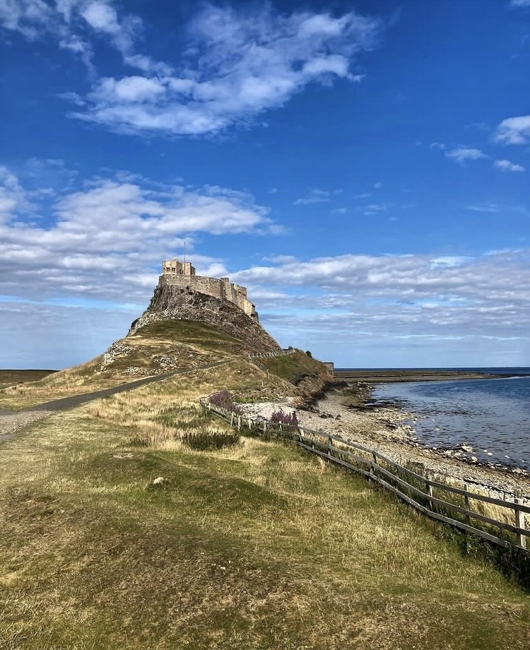 Distanced view of castle on a hill by the sea with bright blue sky above.