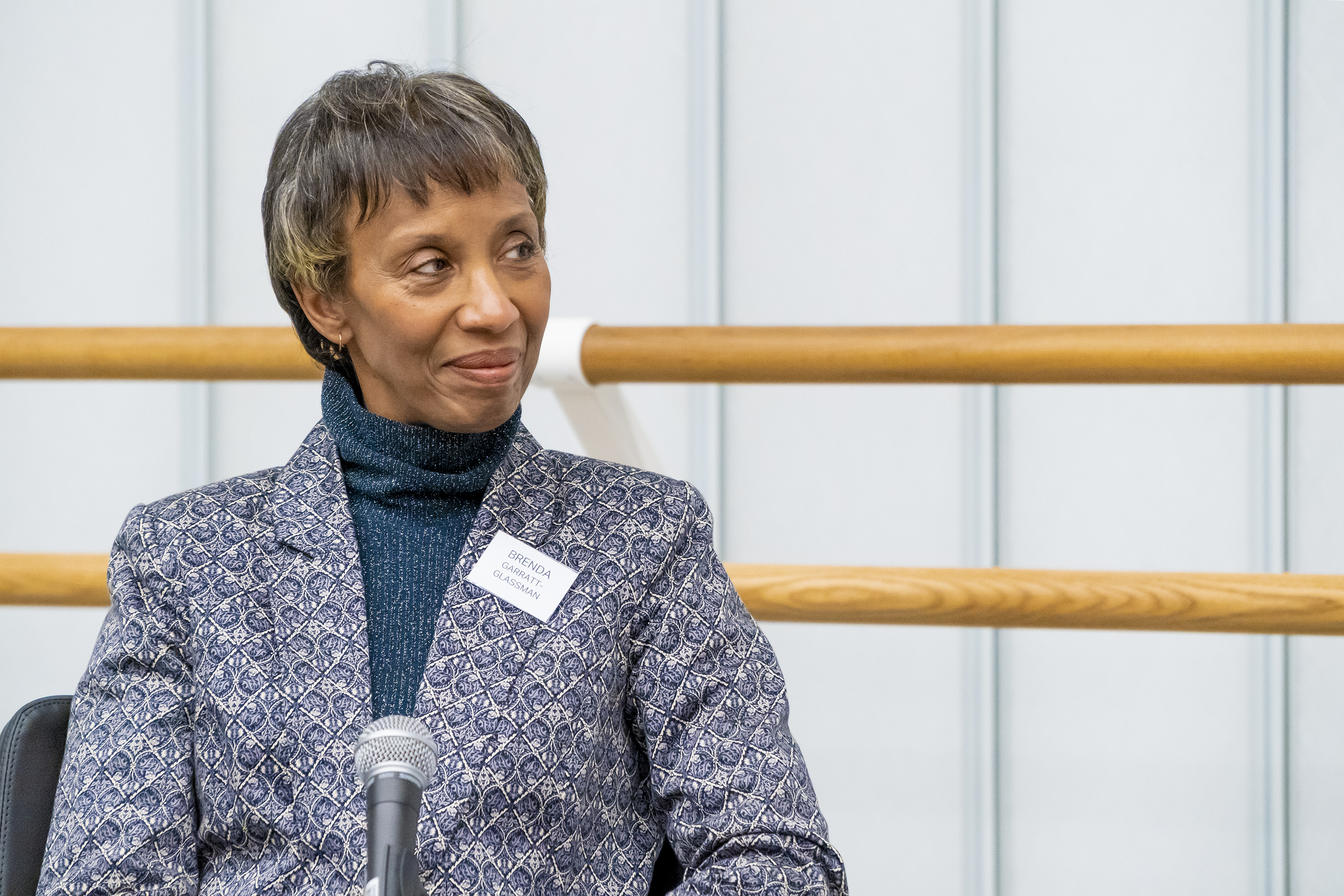 Black woman with short grey hair sat in front of a ballet barre.