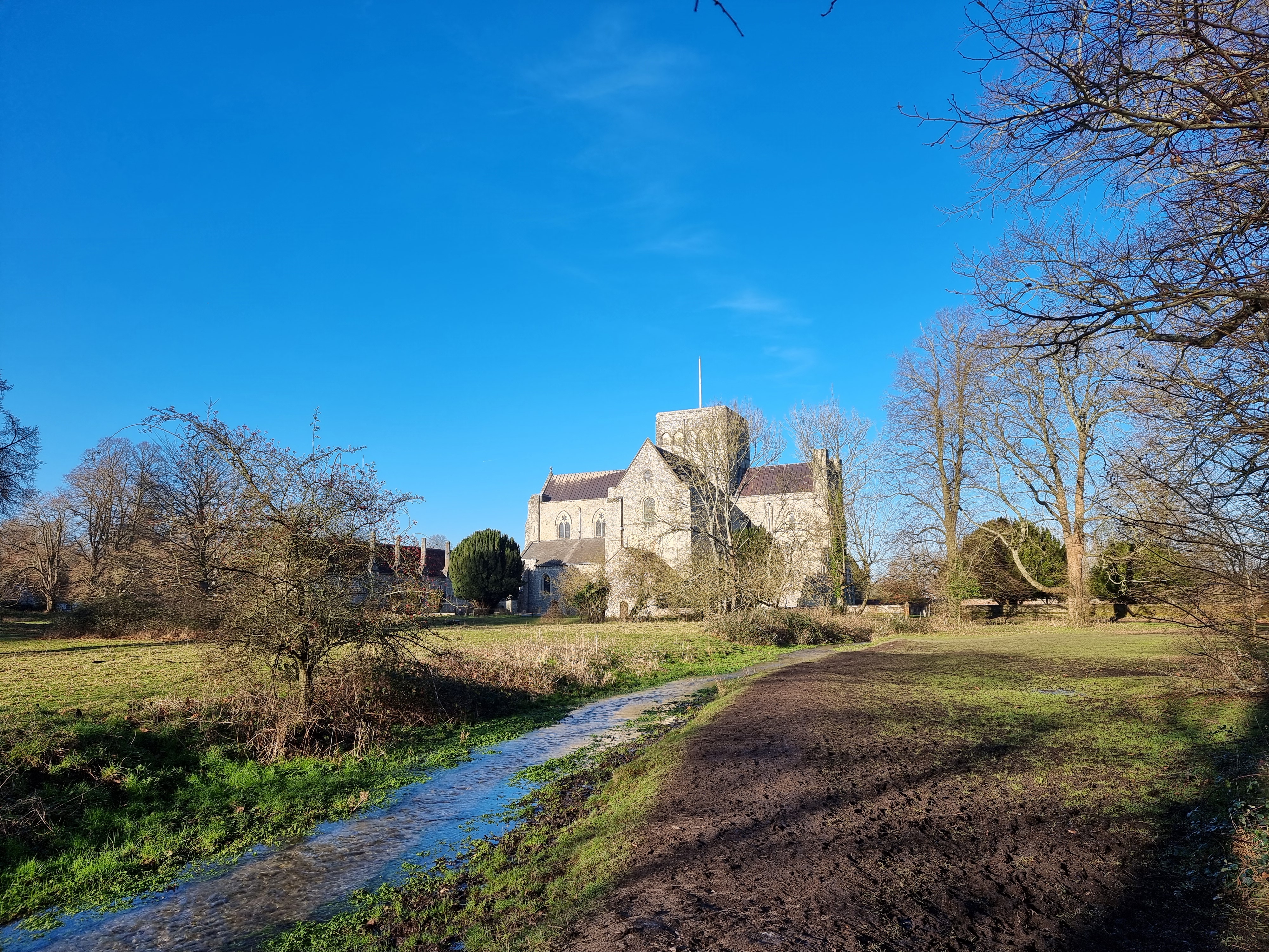 Green fields with a small stream leading to a stone church on a sunny day.