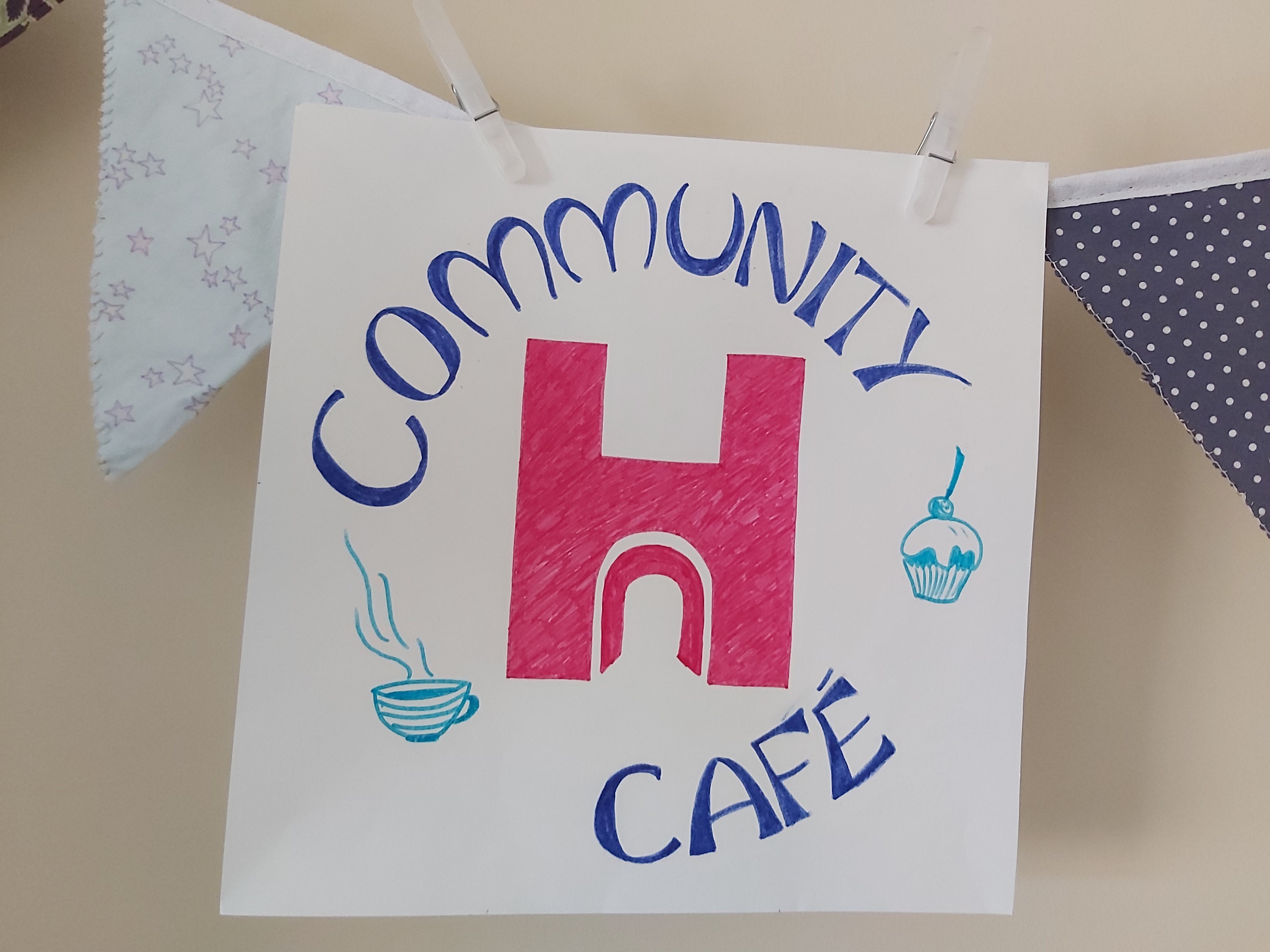 Hand-drawn square sign for Community Cafe, with pink H logo.