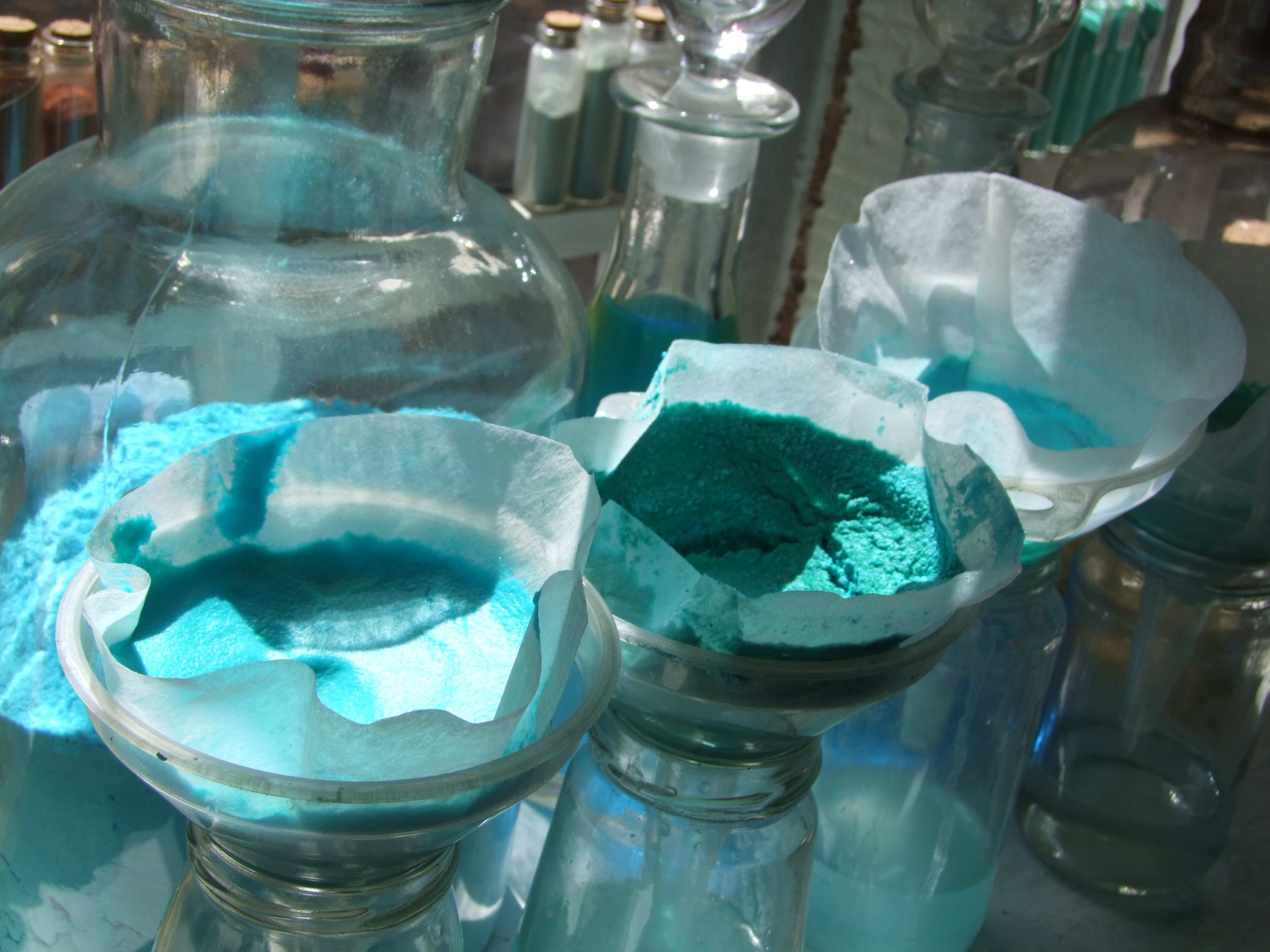 Blue paint pigment drying atop filter paper funnels in glass jars.