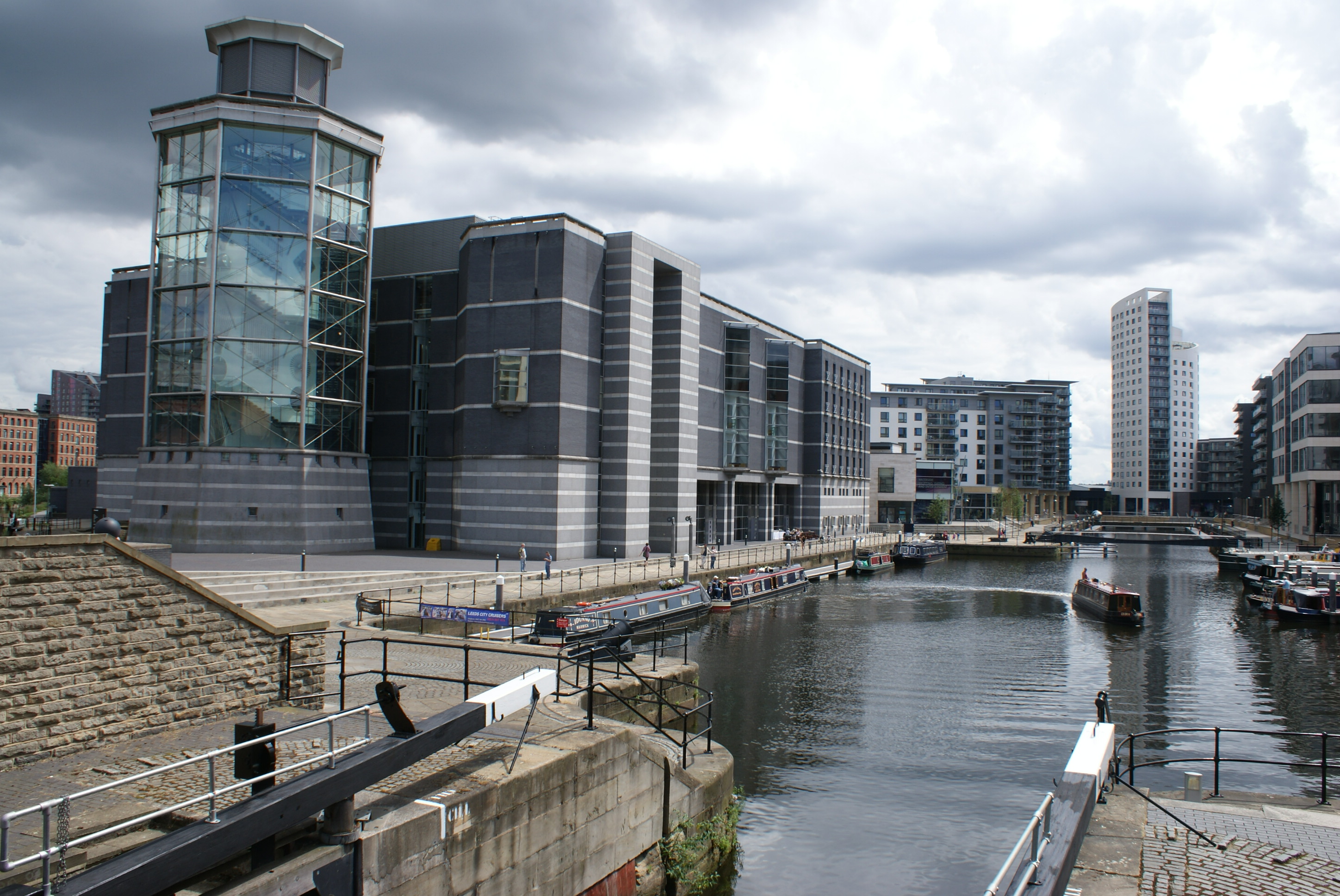 View across urban canal of large 5 storey modern grey building with hexagonal glass tower at one end.