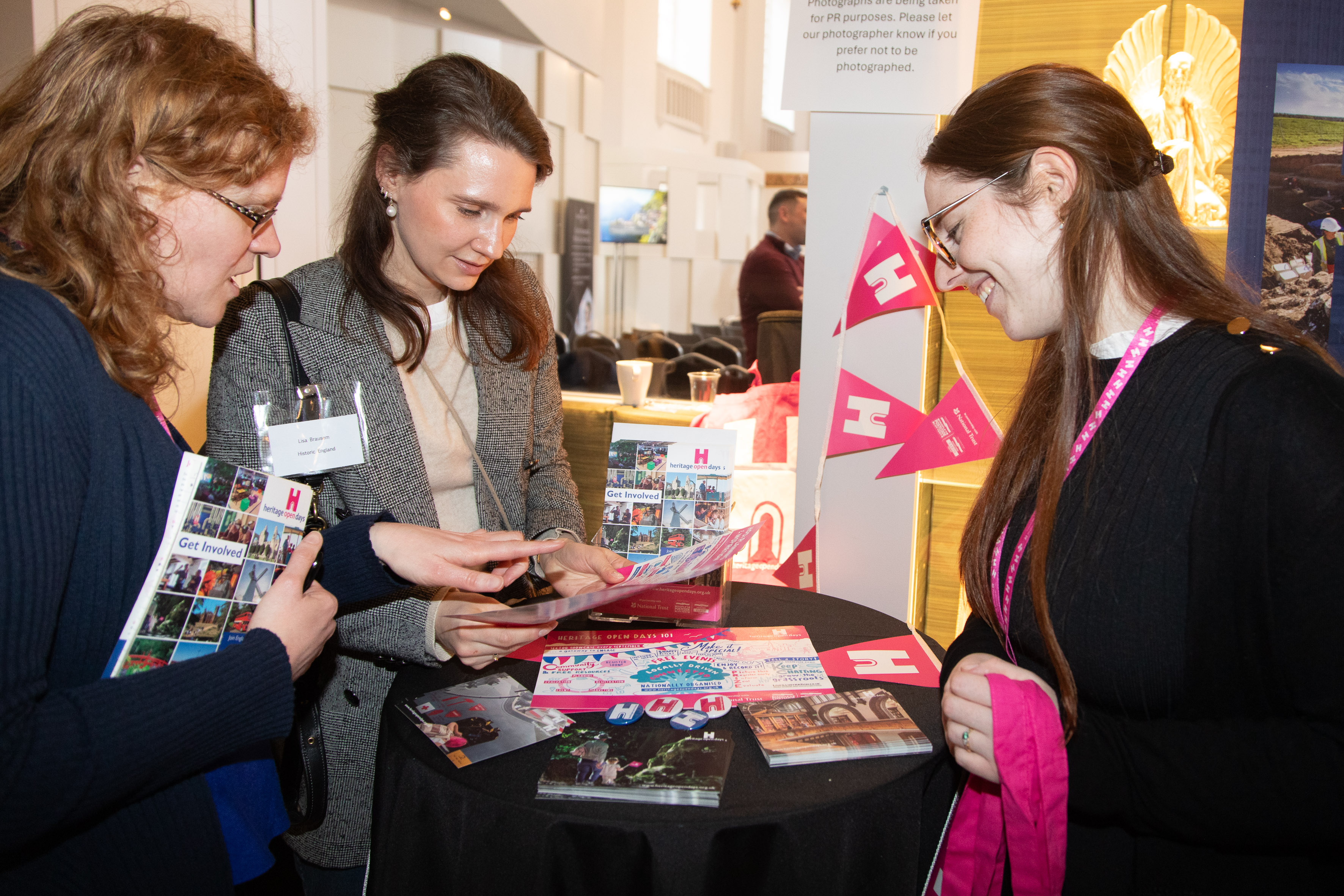 Three women looking at and discussing leaflets on a small poseur table.