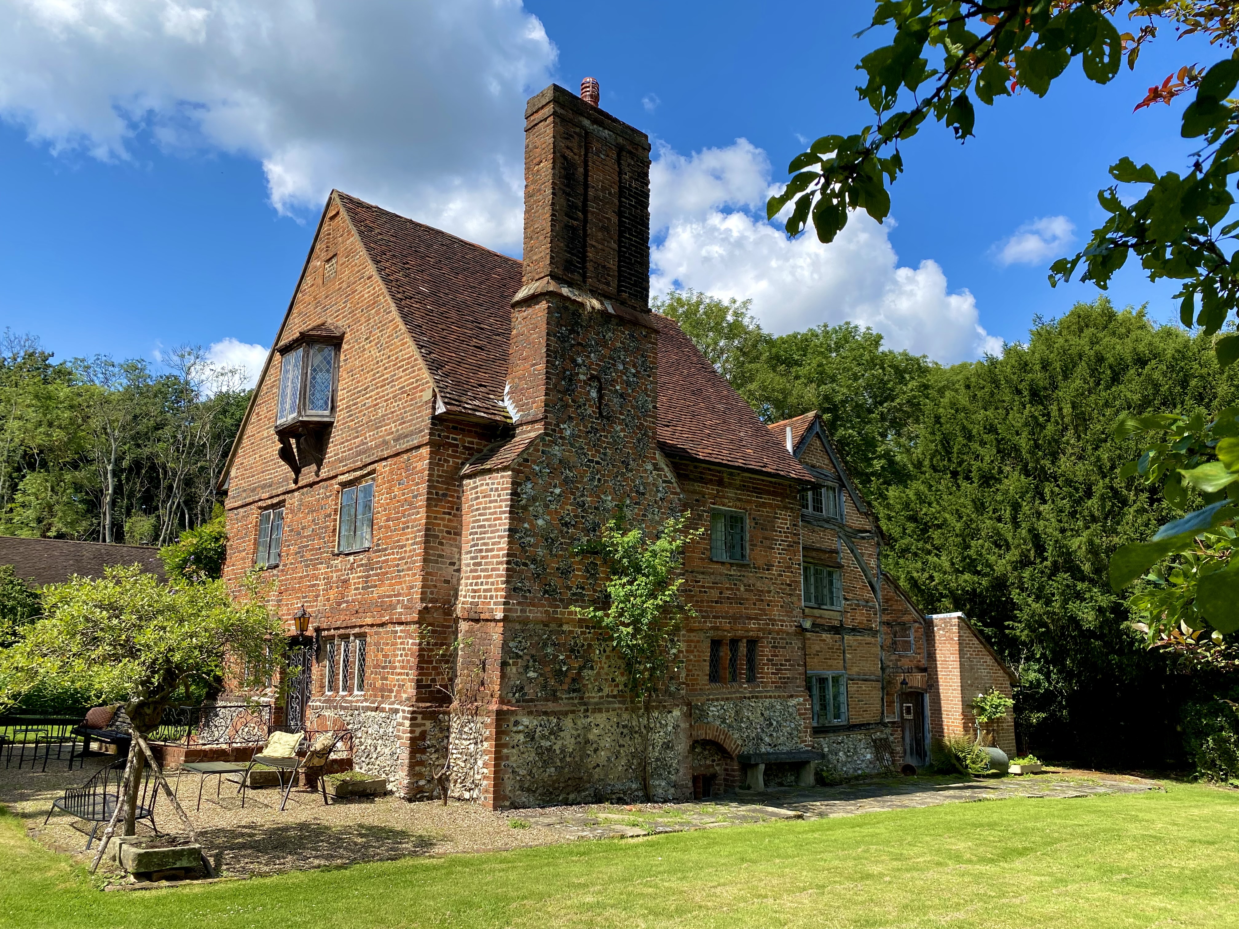 Quirky old 3 story brick house with large chimney set within green lawn and woodland.