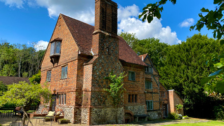 Quirky old 3 story brick house with large chimney set within green lawn and woodland.