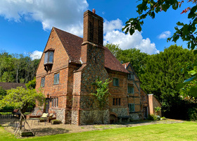 Quirky old 3 story brick house with large chimney set within green lawn and woodland.