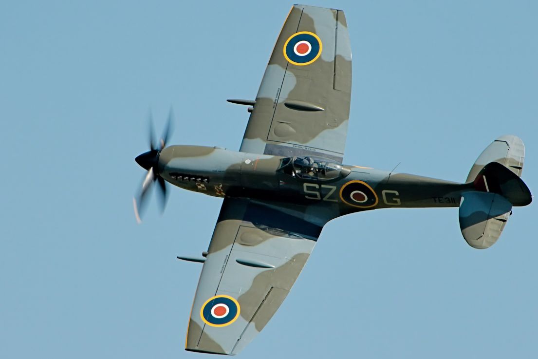 A spitfire plane flying through the sky, it's propeller turning in a blur.