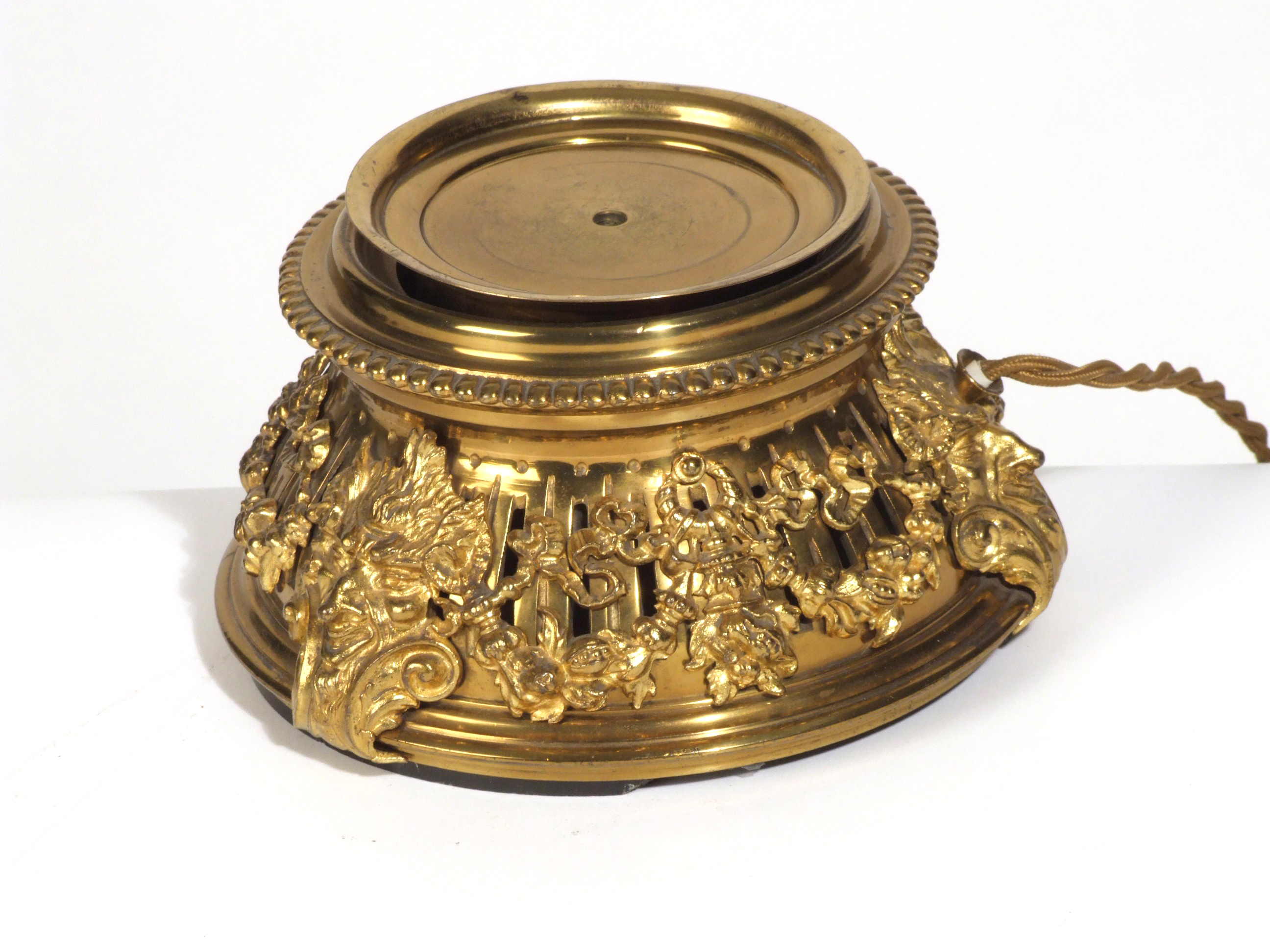 Small, round, ornate gold metal stand with a wire trailing from it.