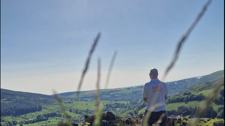 Man looking out over a wide gently hilly landscape.