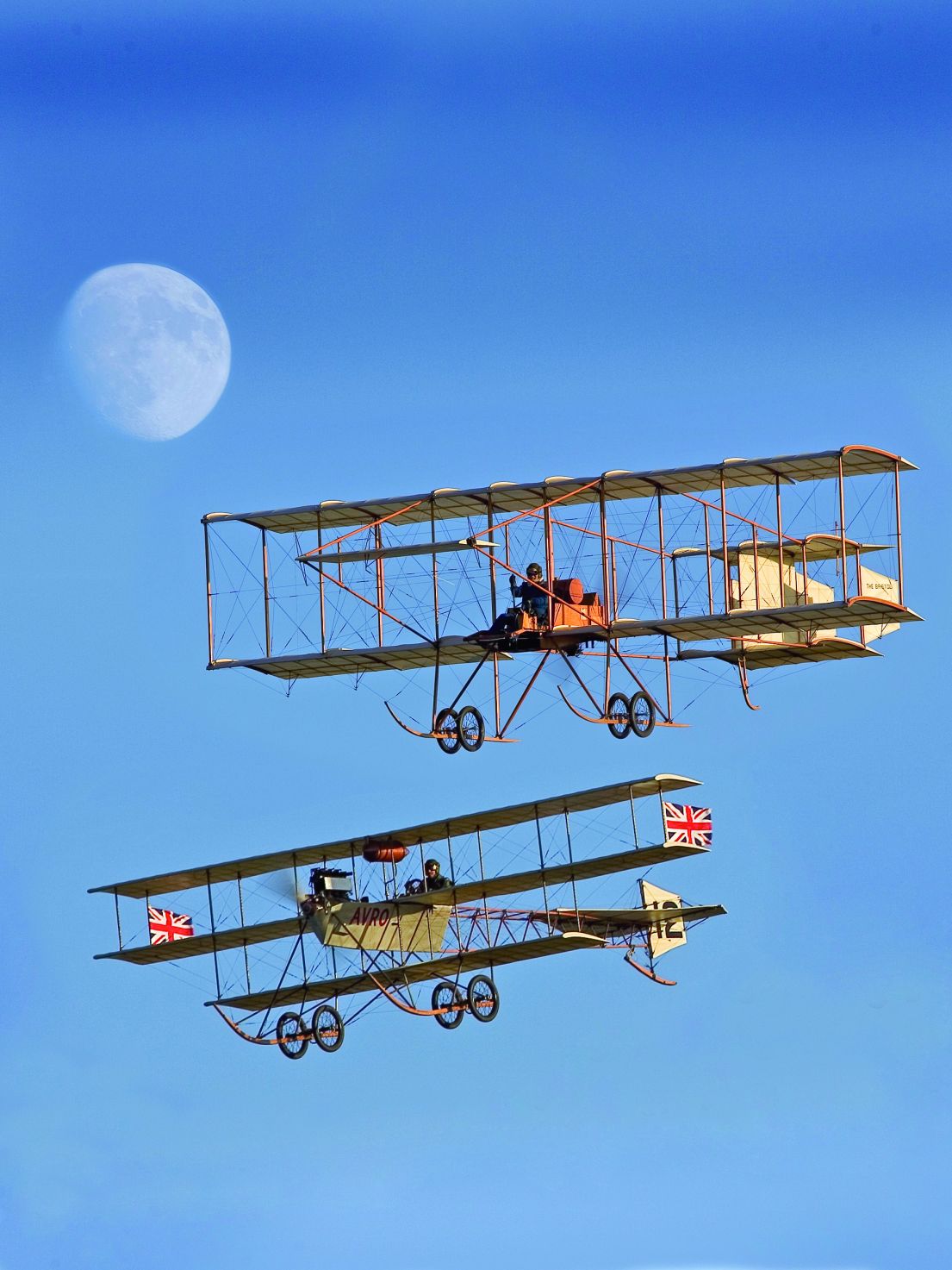 Two Edwardian Plans, made from wood and cloth, flying one on top of the other through a blue sky.
