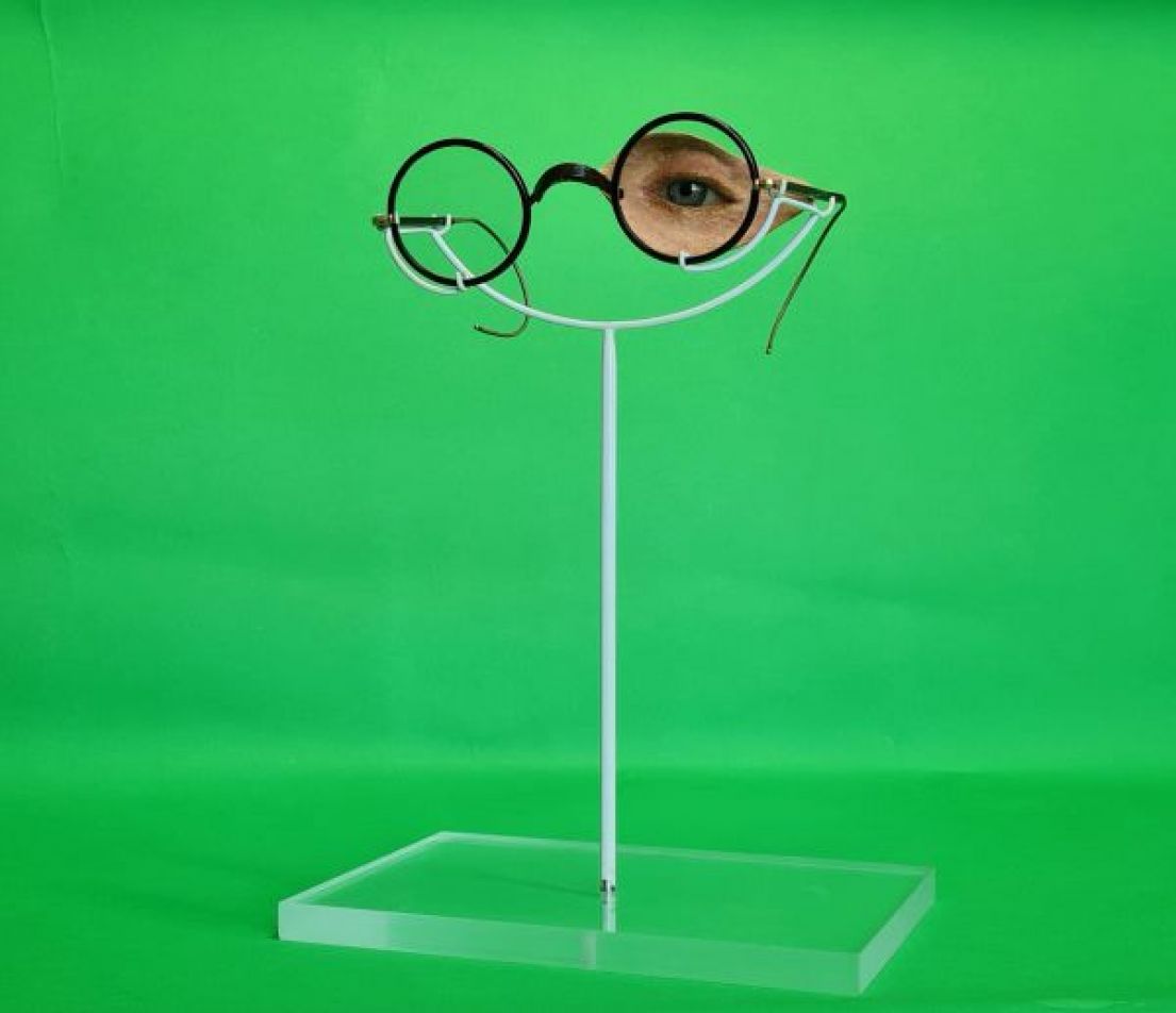 A displayed prosthetic part of a face with an eye, positioned behind circular rimmed glasses