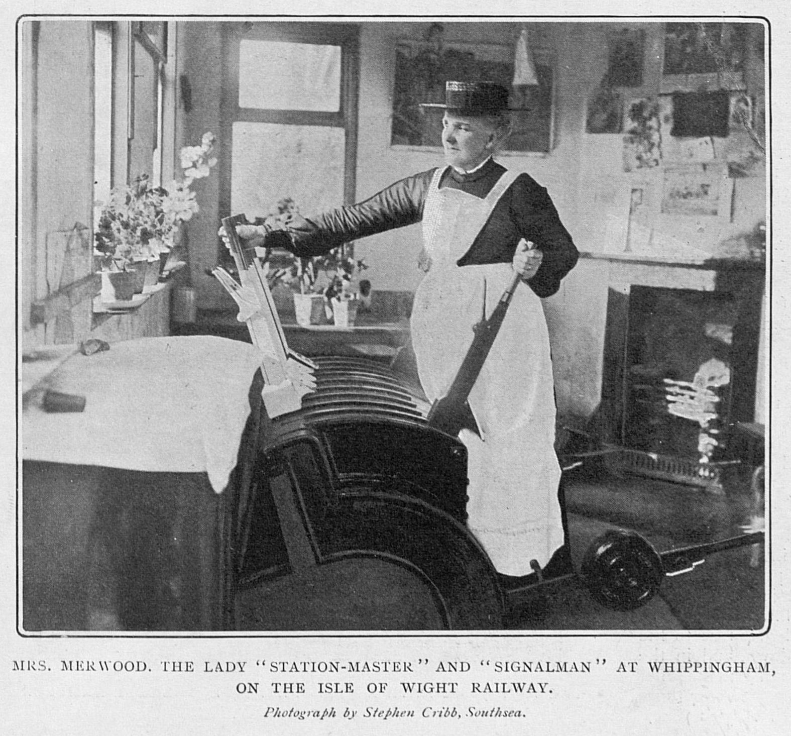 Woman in long white apron and cap operating the levers in a railway signal box.