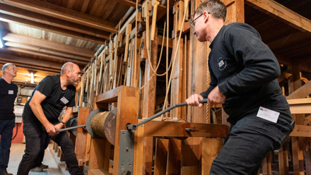 Two men working stage machinery to wind a series of ropes.