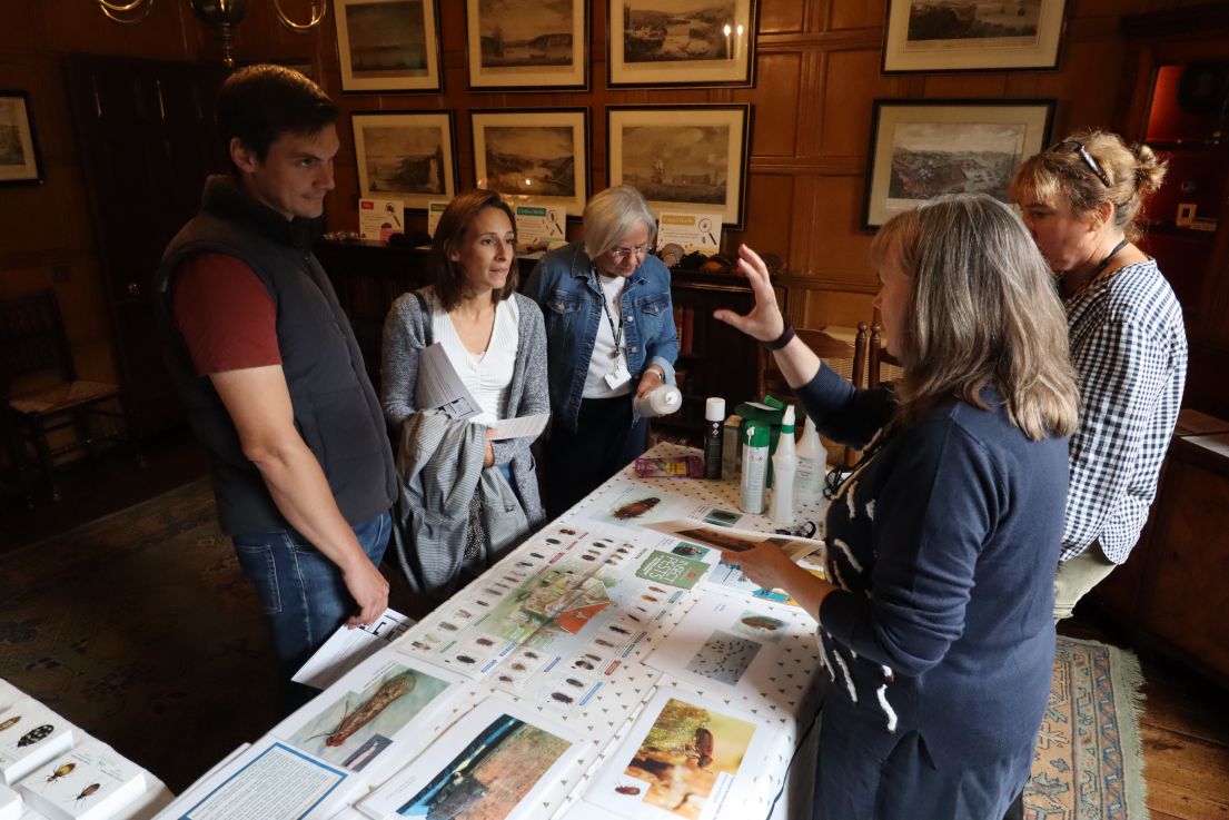 Two curators standing behind a table discussing the artefacts laid on the table to three visitors.