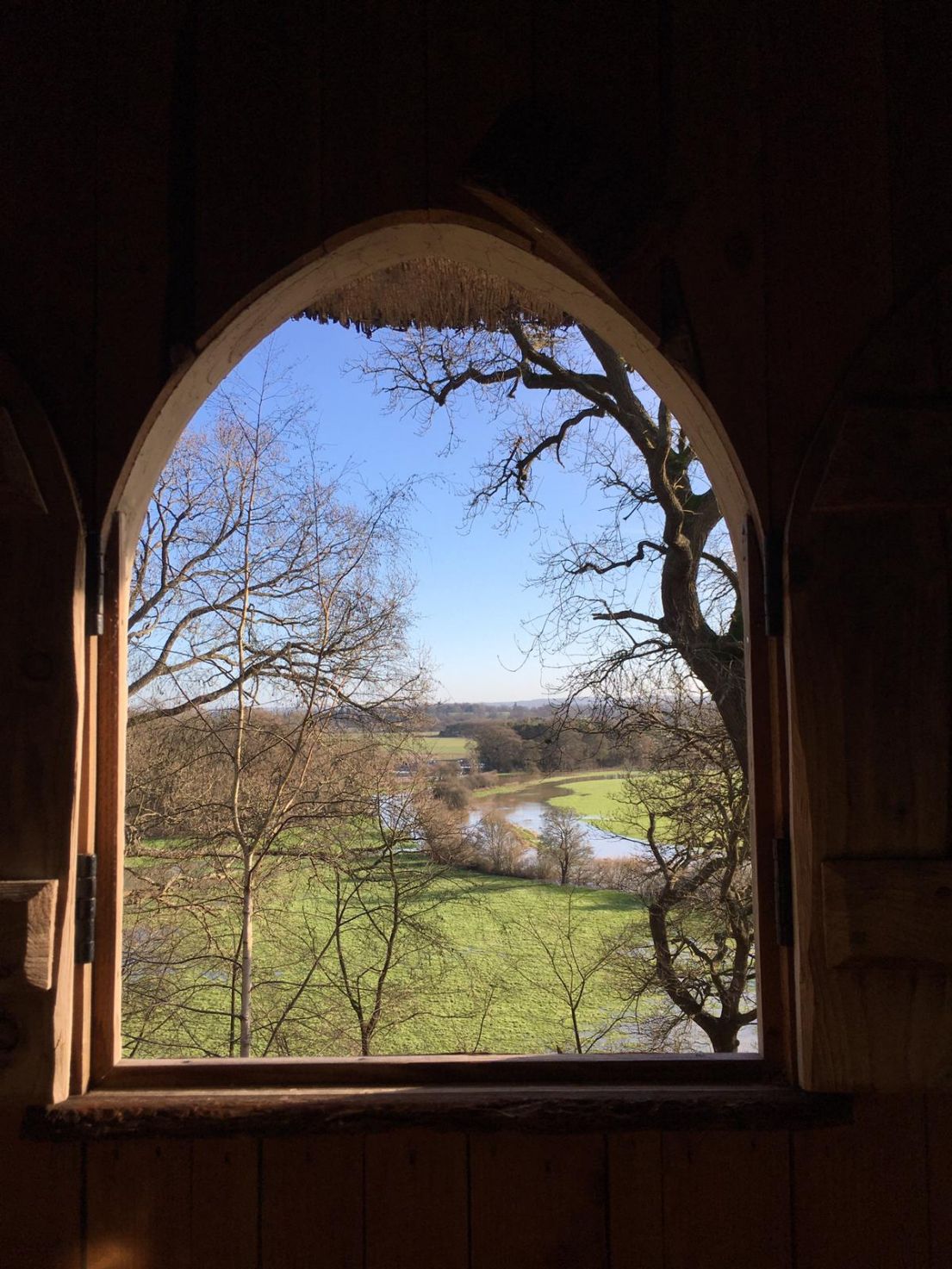 Looking out an open arched window to a wintery garden with bare trees.