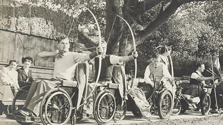 Old photo of young men in wheelchairs lined up shooting arrows from longbows.