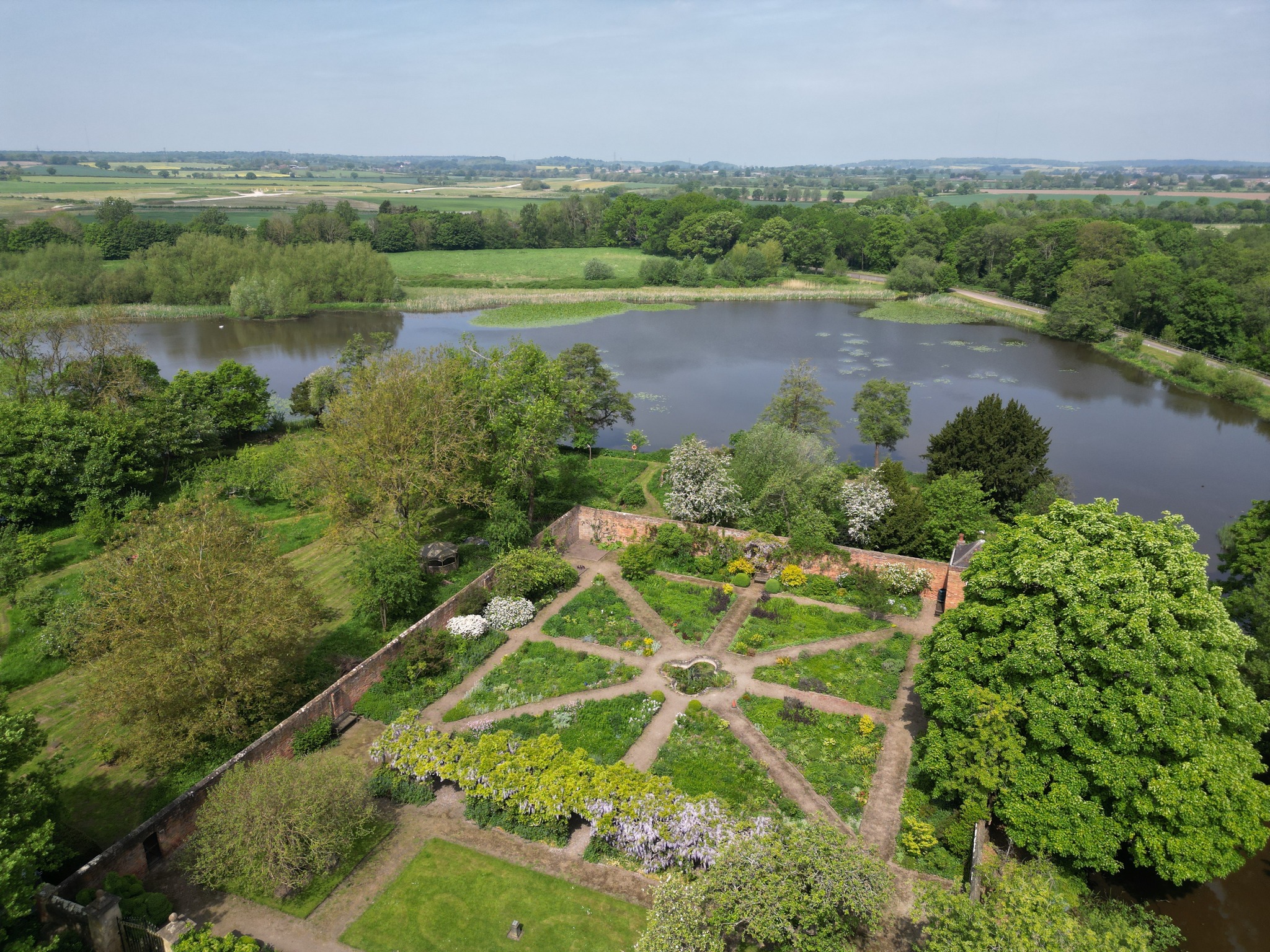 Aerial view of a garden laid out in a radiating pattern, surrounded by trees with triangular lake behind it.