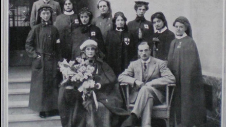 A black and white image of doctor and nurses in cape coats outside a building. Two of the individuals are sat and the others are gathered around on.