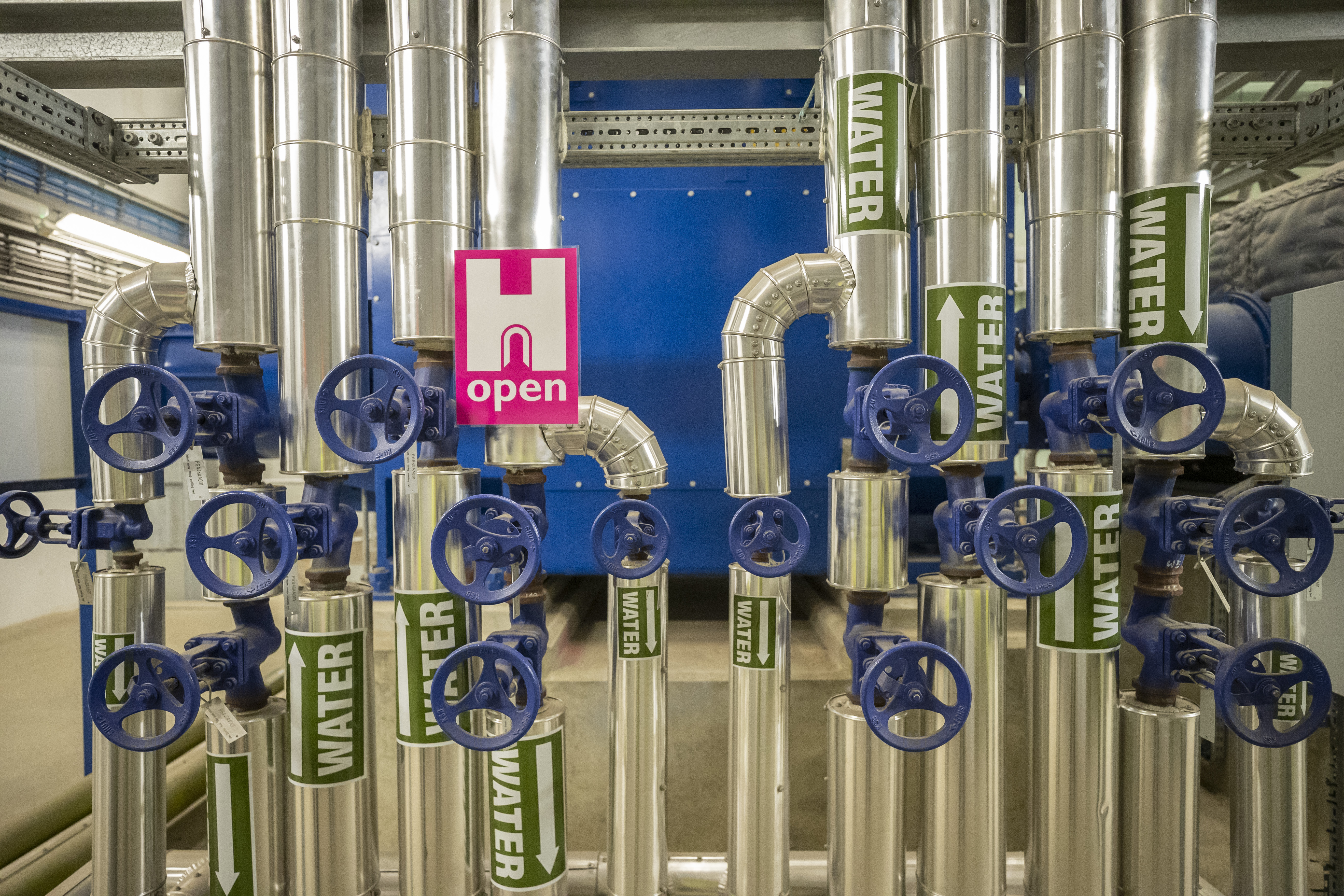 Industrial metal piles with blue wheels that open valves. A pink H Open Heritage Open Days Poster.