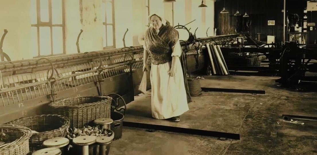 A re-enactor dressed as a mill worker, surrounded by wicker baskets.