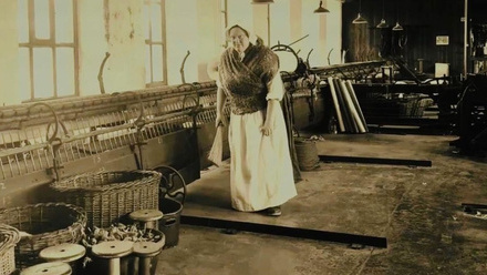 A re-enactor dressed as a mill worker, surrounded by wicker baskets.