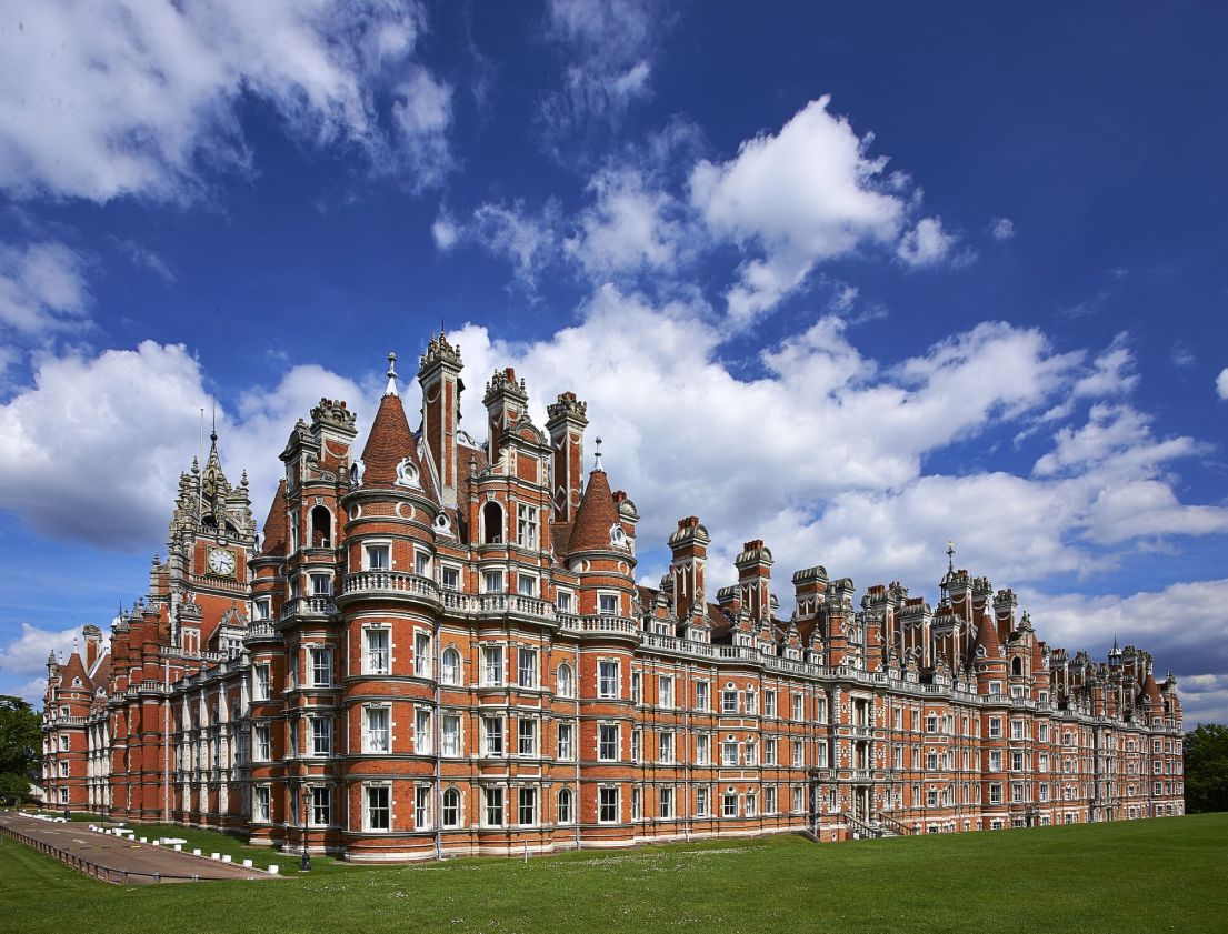 A grand French-Renaissance-style building, the large green lawn at the front and the blue sky dotted with white clouds.