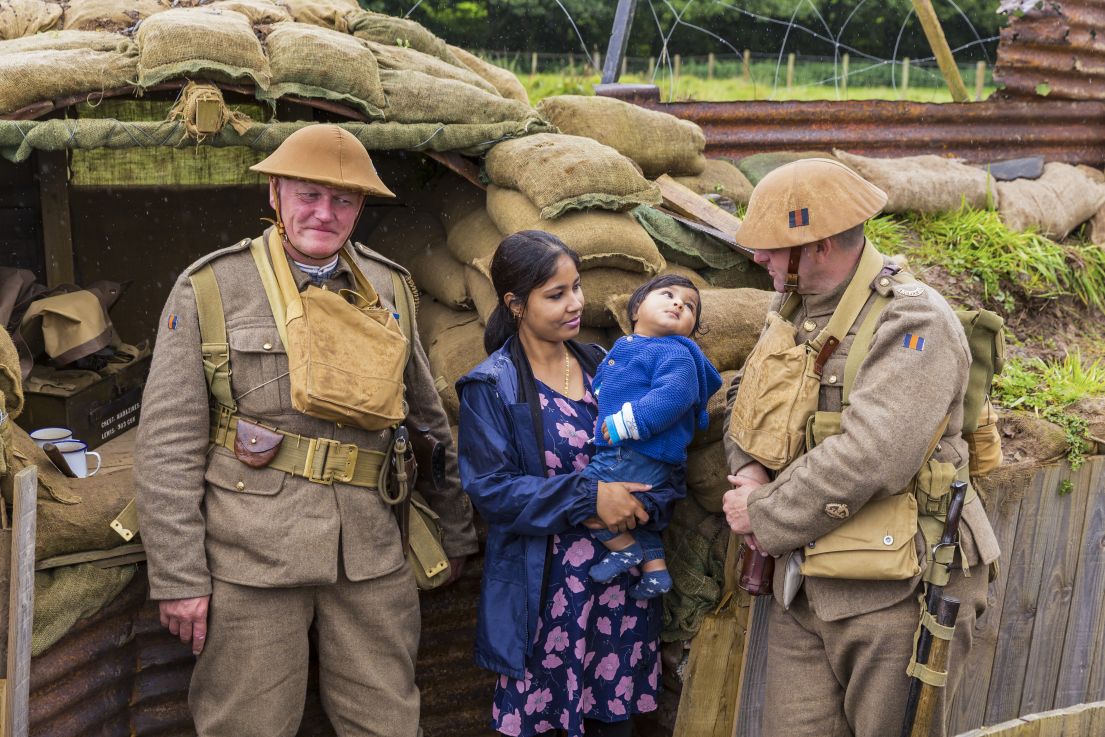 Two men, dressed in light brown WWI army uniform, standing with a women and child in a replica of the trenches.