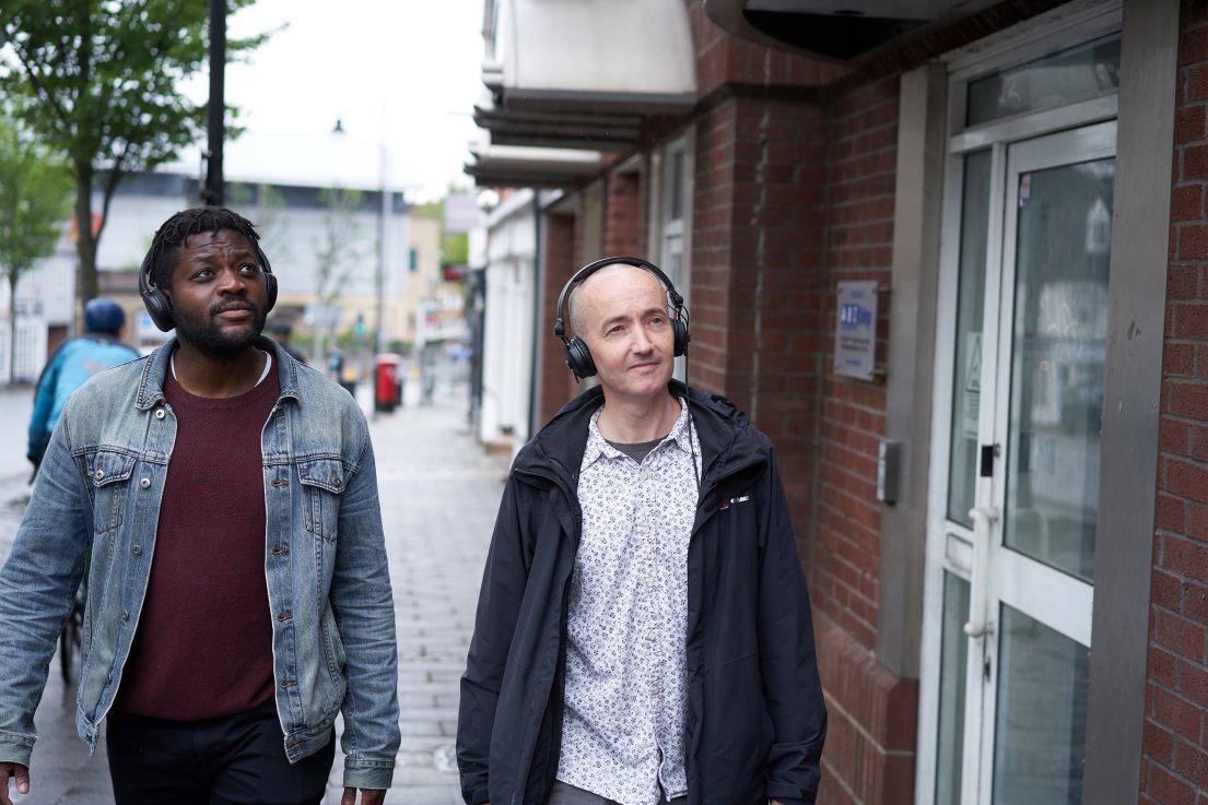 Two men on a soundwalk, both wearing black over-ear headphones