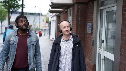 Two men on a soundwalk, both wearing black over-ear headphones