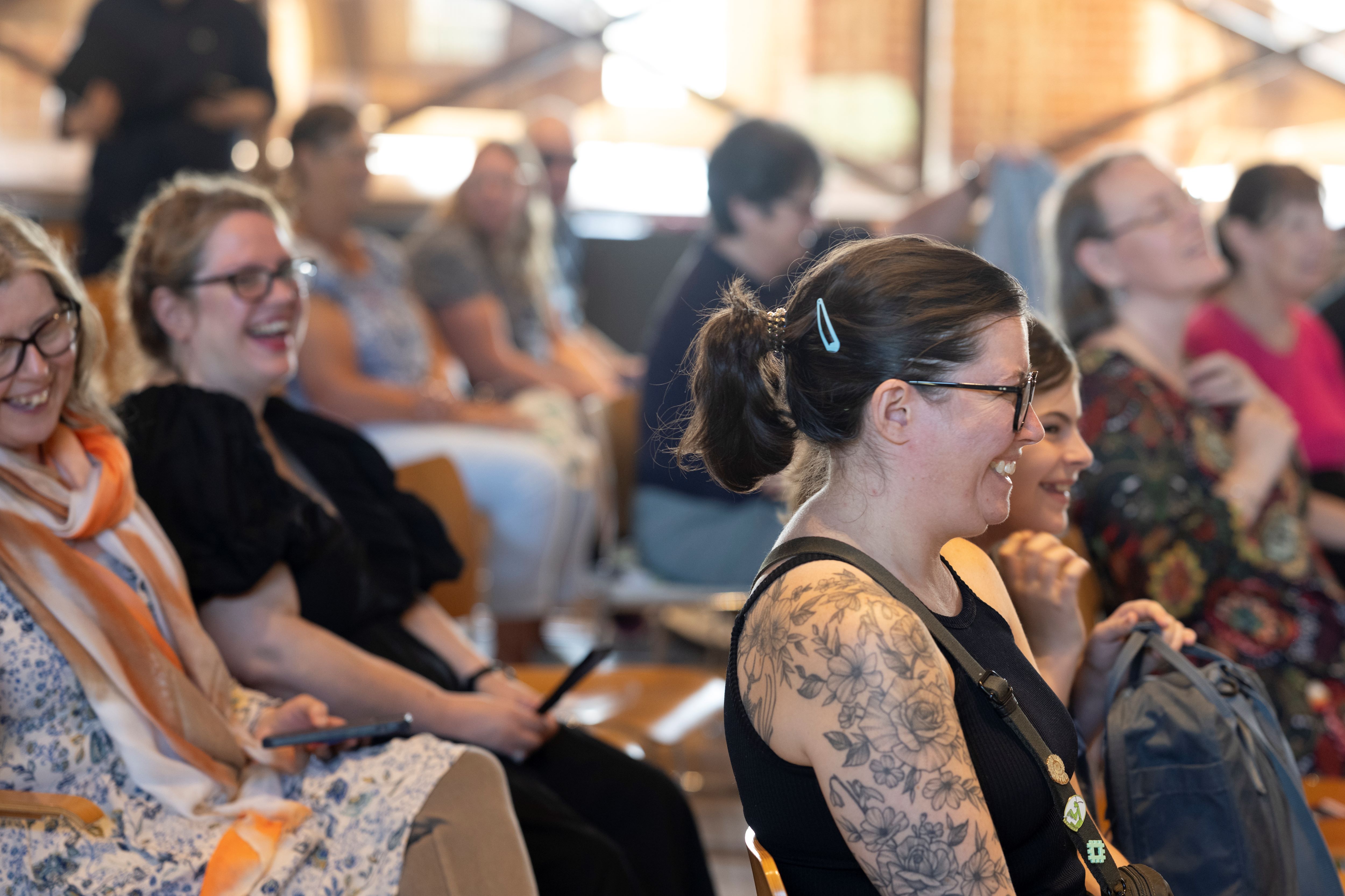 Crowd of people sat smiling and laughing at a talk.