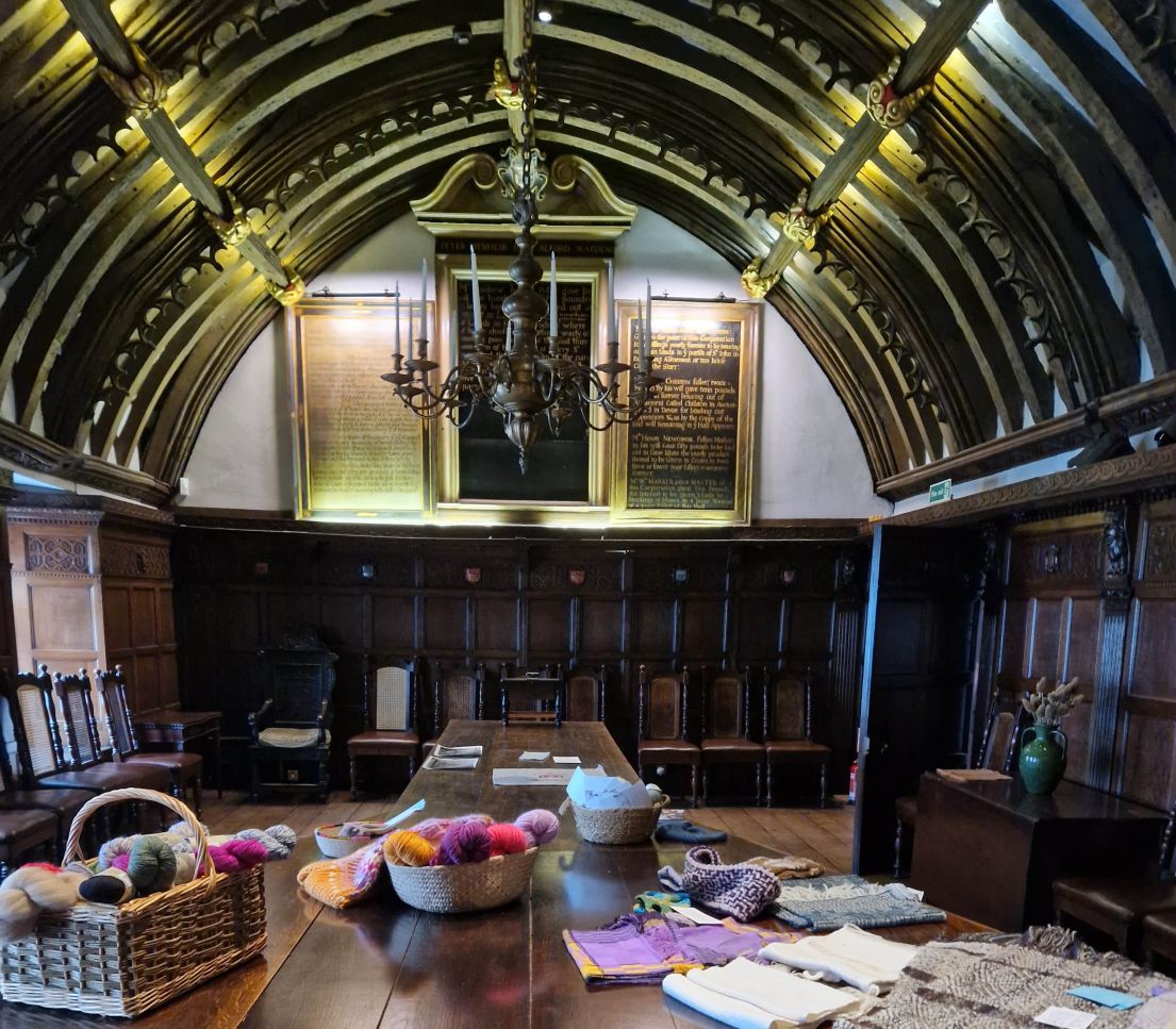 Dark wood panelled hall with arched ceiling. Table in the centre with woollen craft materials scattered on it.
