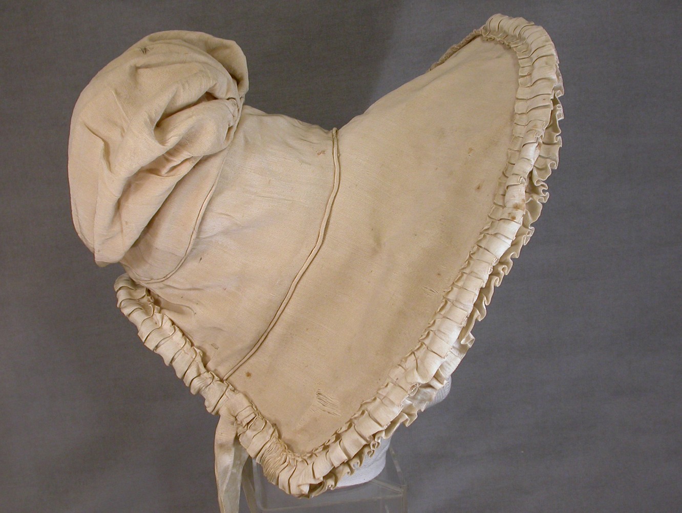 Cream silk bonnet with high front peak, pleated ribbon trim and a puffed crown.