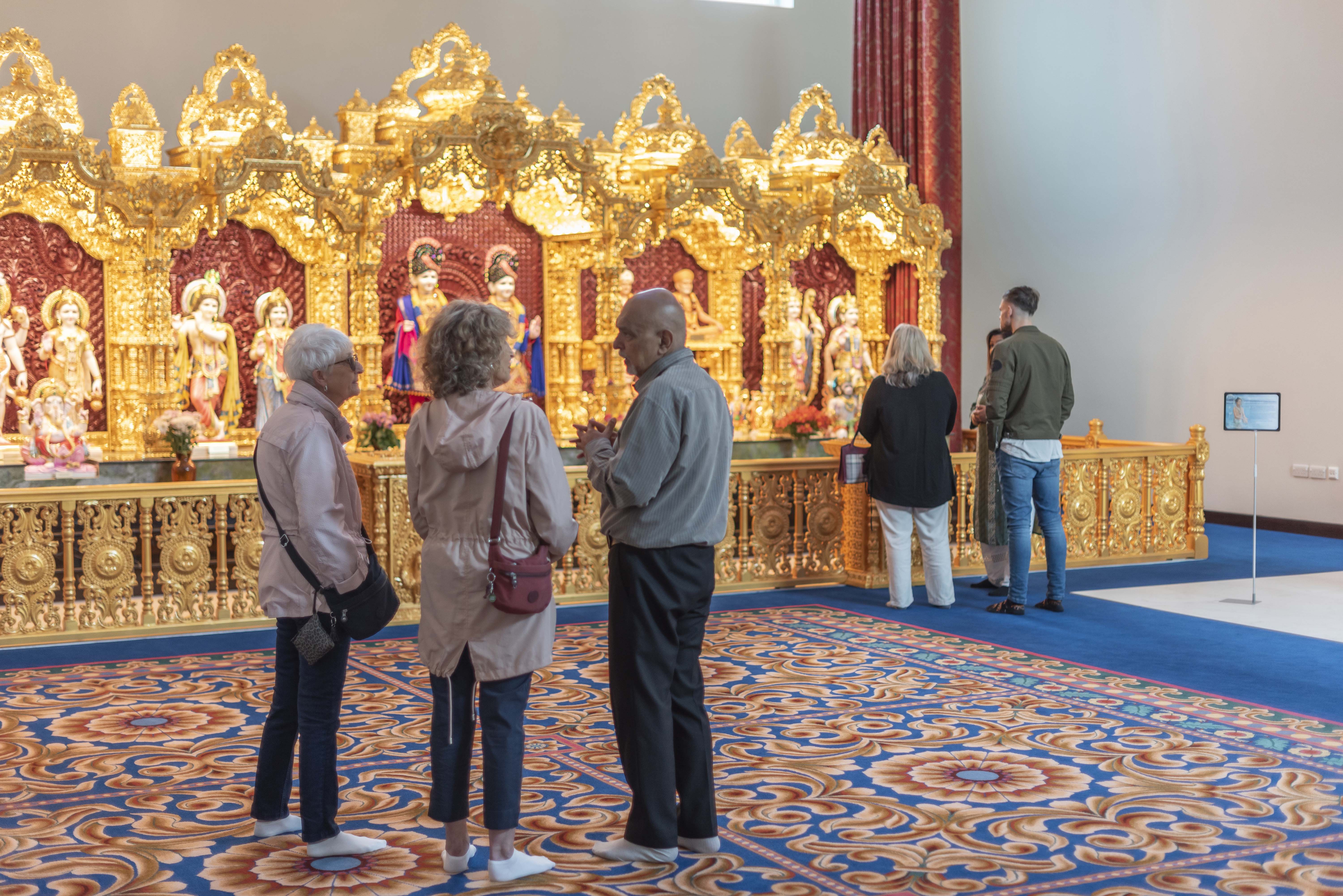 Two small groups of people in a large room with brightly patterned carpet and golden shrine at one end.
