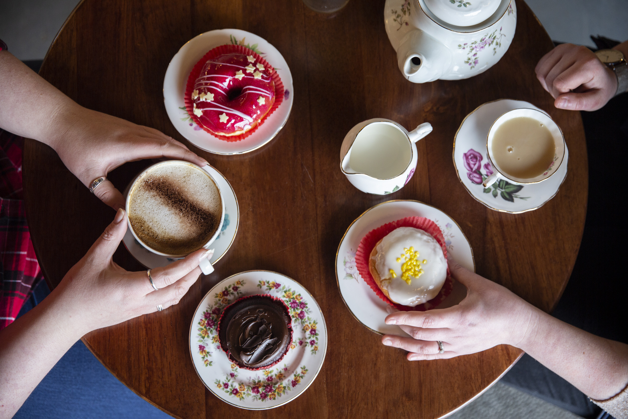 Birds eye view of two people having tea and sticky buns at a round wooden table.