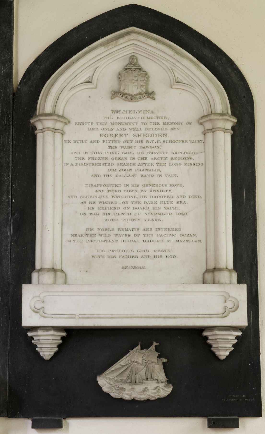 A white marble plaque dedicated to someone's beloved son, Robert Shedden, who died at sea. 