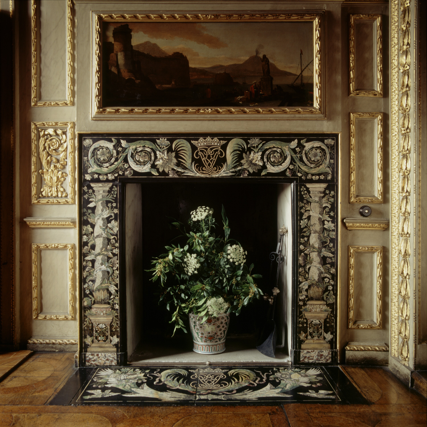 Ornate fireplace with vase of cream flowers in its hearth. The surround has cream coloured carving on a black background.