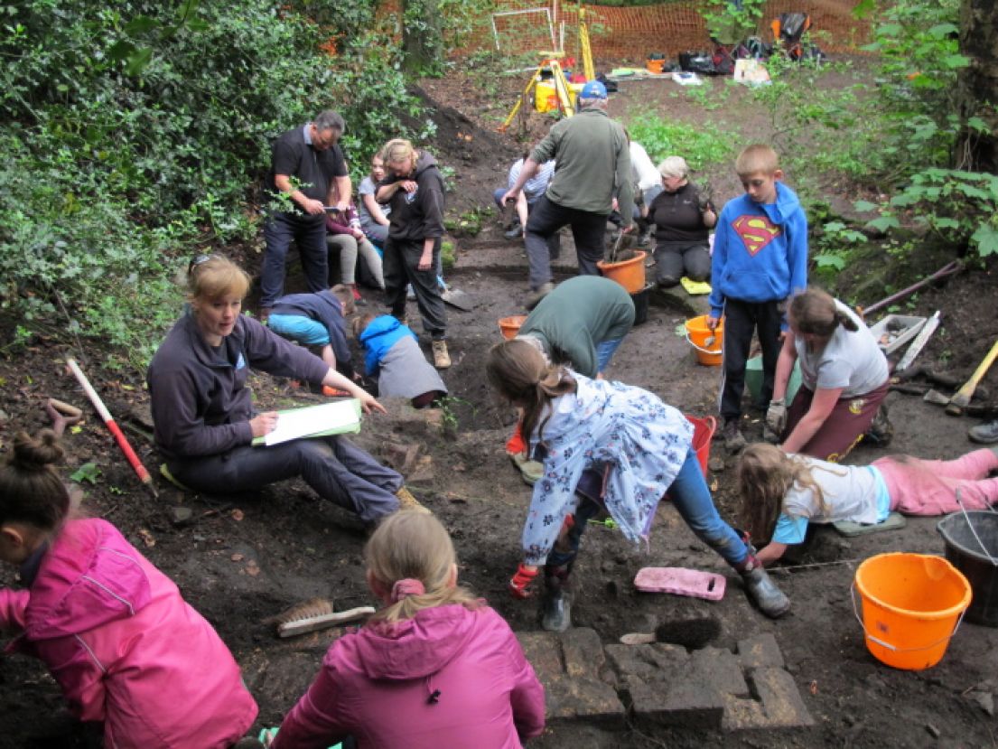 A group of primary school aged children working on an archaeological dig site in the mud.