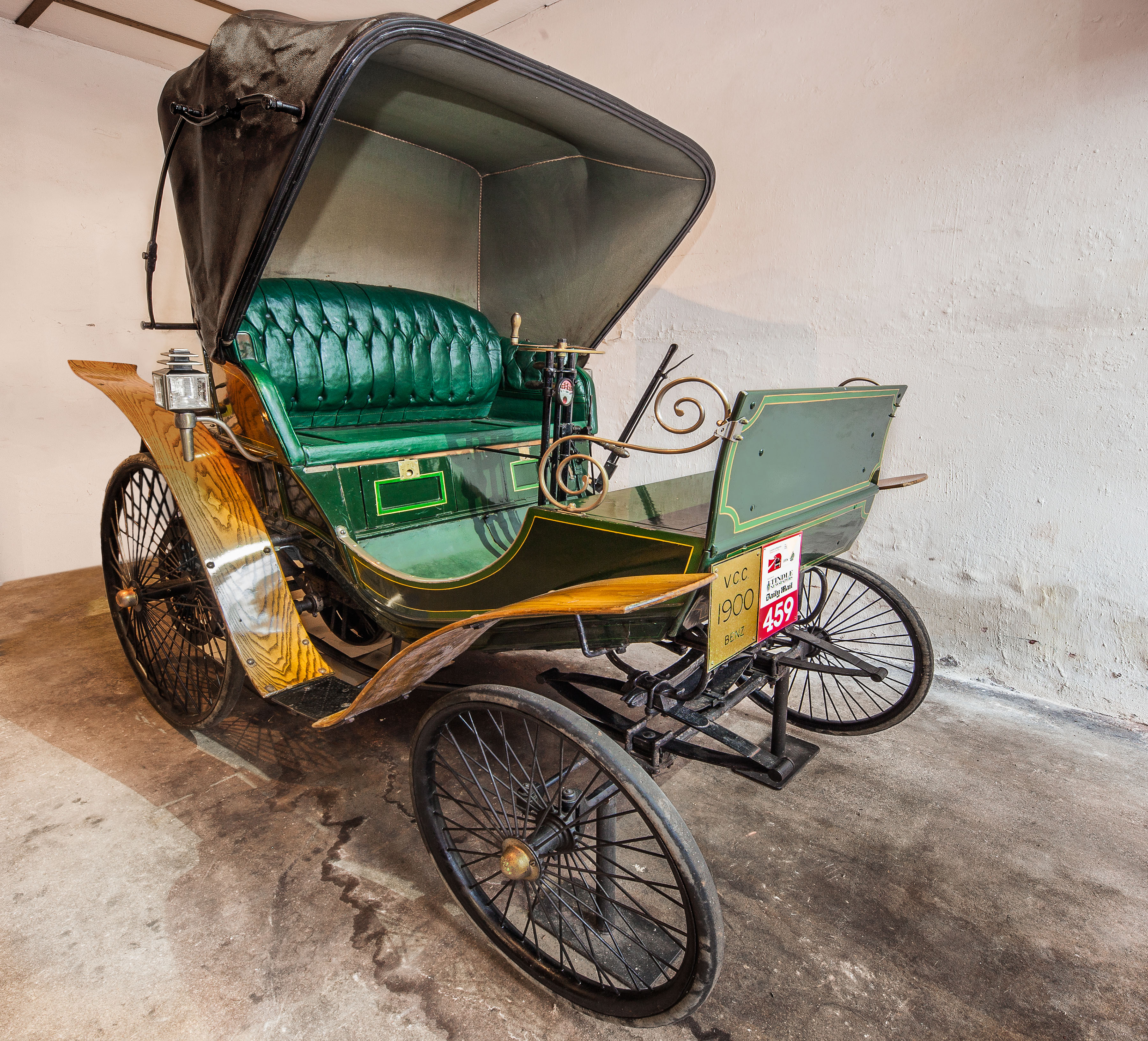 Old car looks like a big carriage / pram with, four big wheels, a hood and green leather seat.