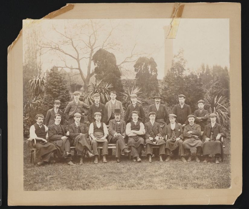 Formal photographic portrait of large group of men in a garden.