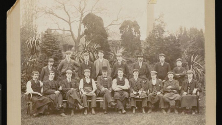 Formal photographic portrait of large group of men in a garden.