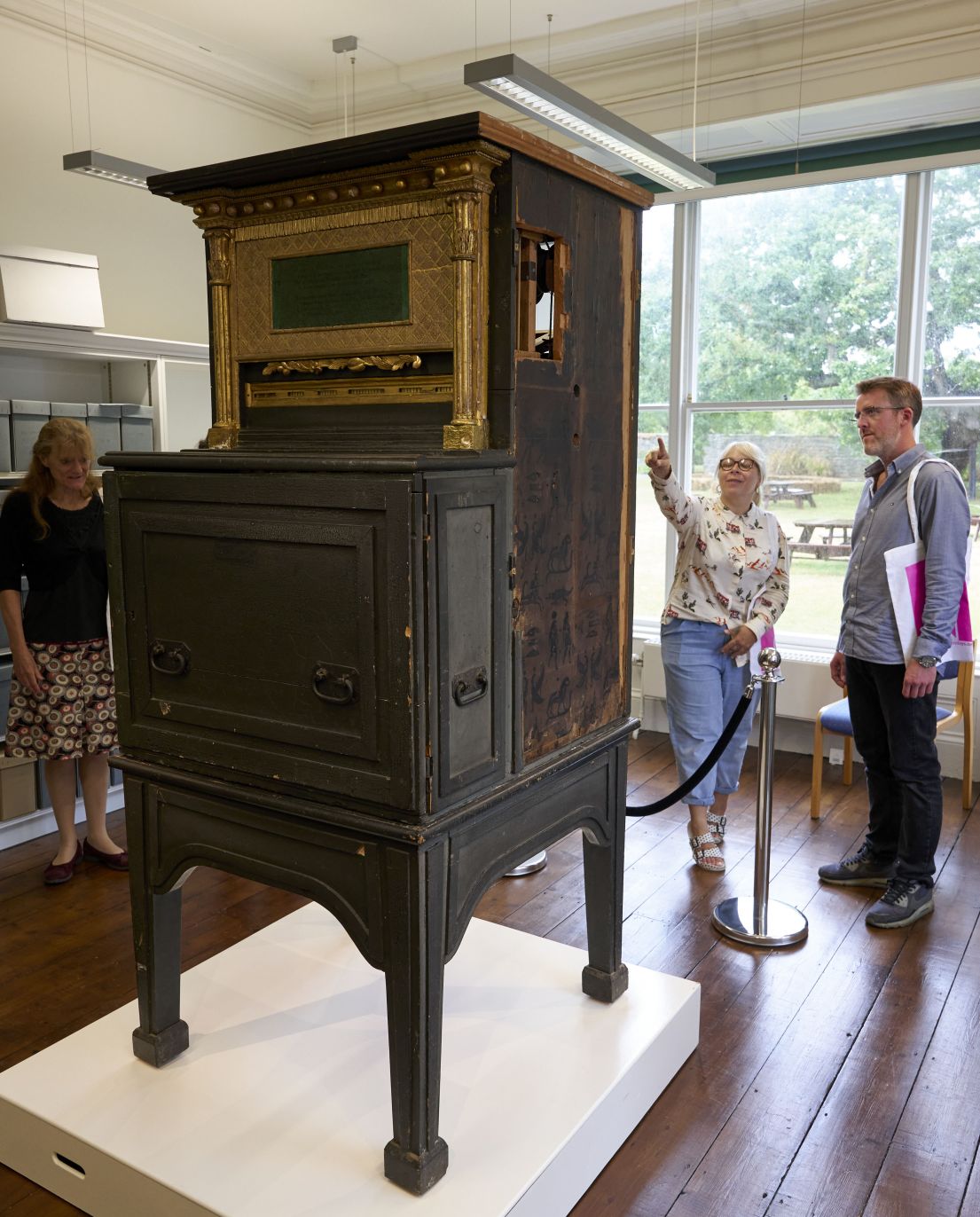 Three people stood around a wooden contraption. On four long feet, the contraption is around 2m tall.