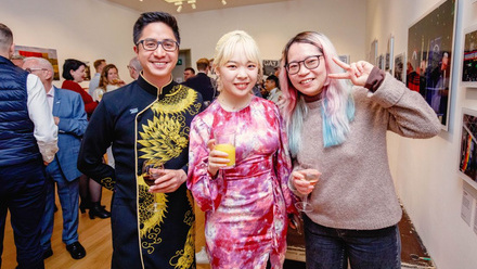 Three individuals from Queer China, dressed in bright colours and all holding drinks and toasting for a picture.
