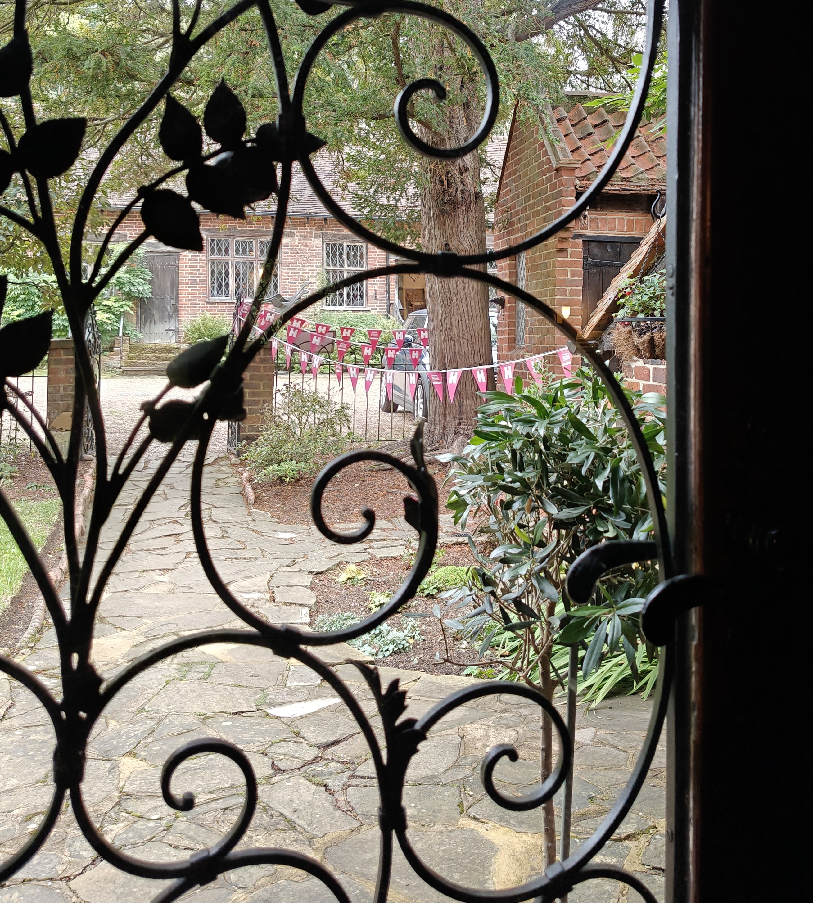 Bunting outside a brick home seen through a decorative iron gate.